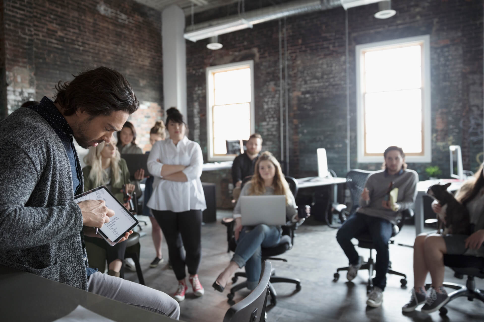 Creative businessman with digital tablet leading meeting in open plan loft office