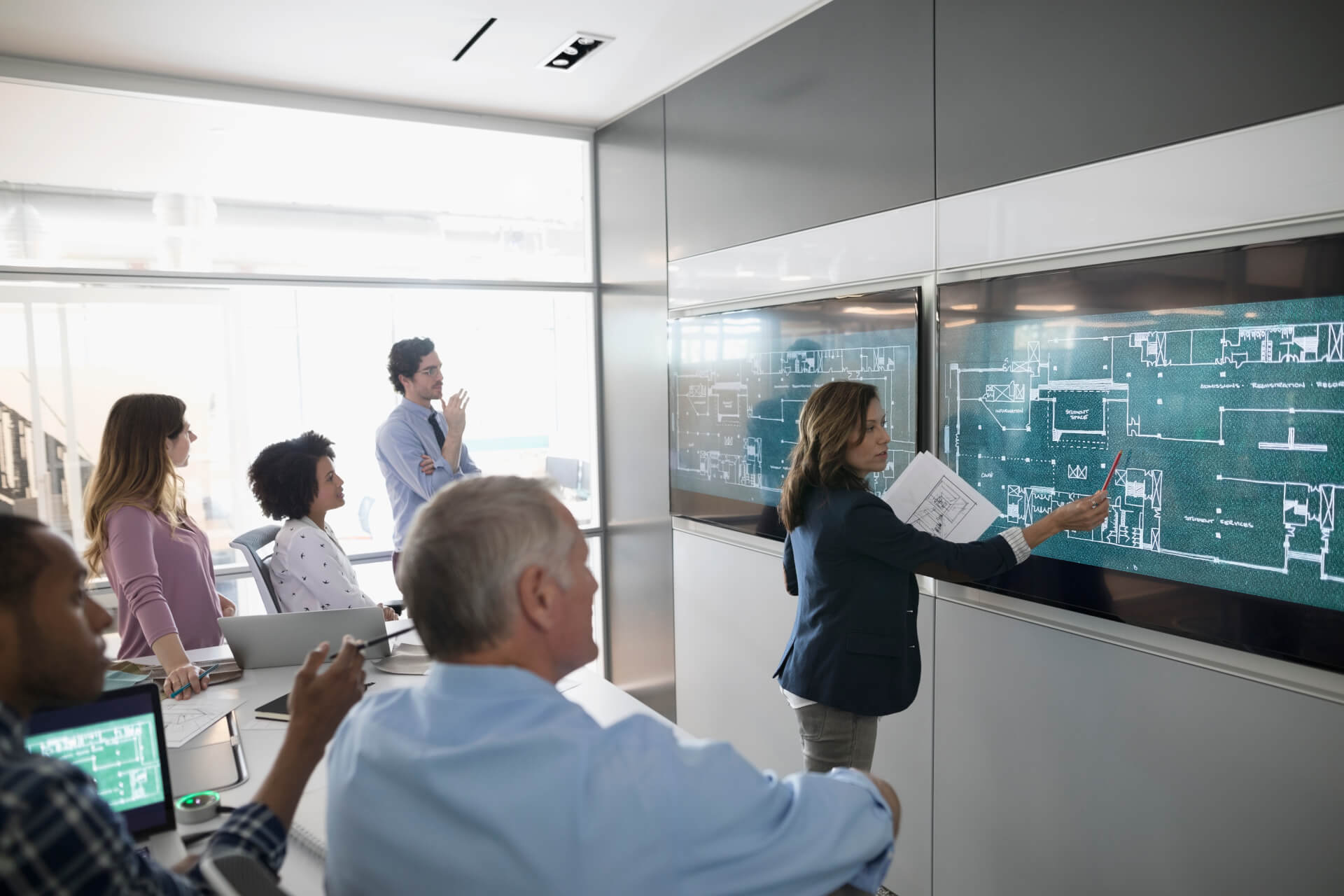 Female architect discussing digital blueprints at screen, leading conference room meeting