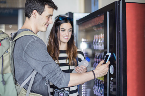 Young couple paying with mobile phone the soft drink at vending machine in the airport.